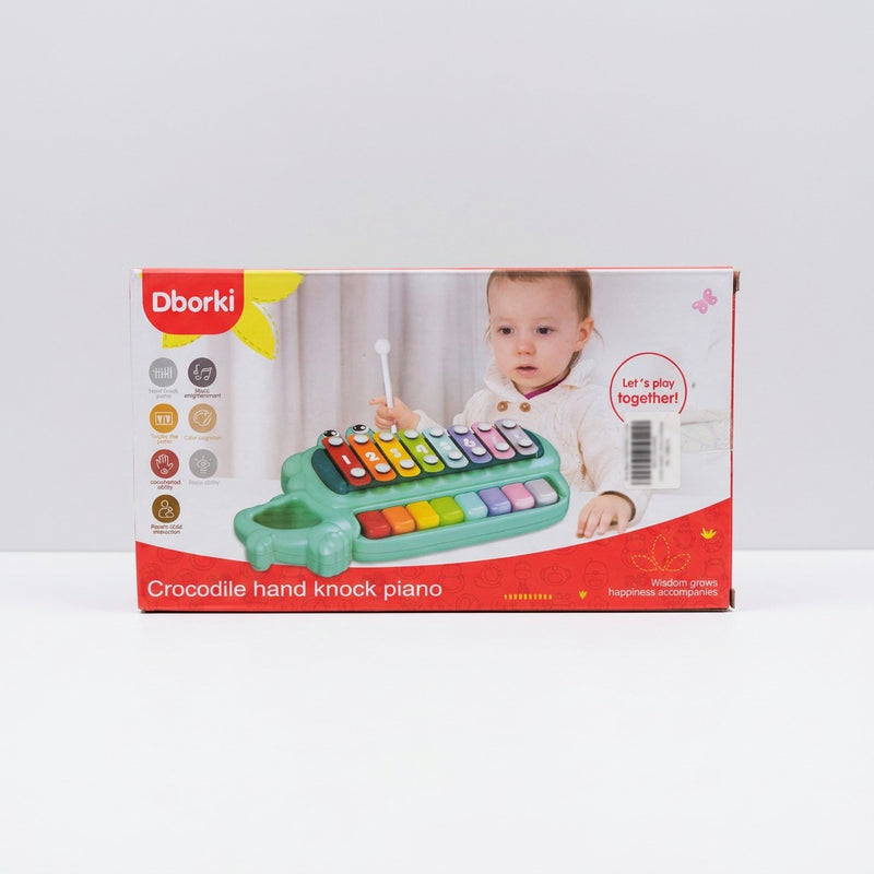 Crocodile hand knock piano in green on its box front, with a child striking the bars