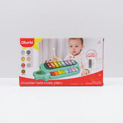 Crocodile hand knock piano in green on its box front, with a child striking the bars
