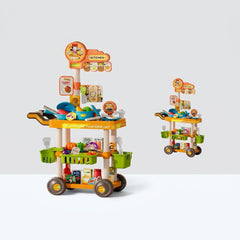 Two-tier wheeled tableware cart with play pots, pans and bowls on top and baskets of play food below, next to its Playhouse Tableware Cart box showing the 69PCS badge