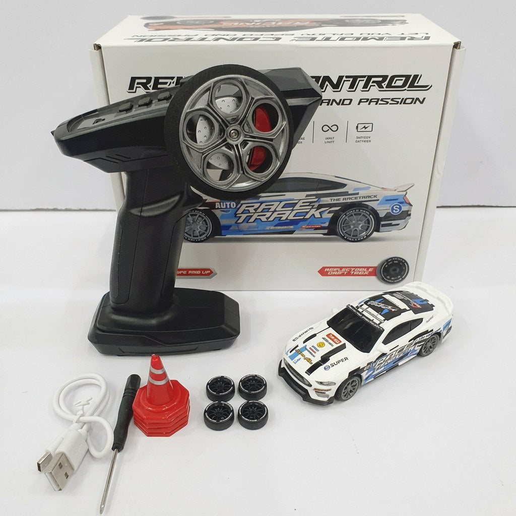 RC drift car beside its box and remote control, with spare wheels, a traffic cone, a screwdriver and a USB cable laid out