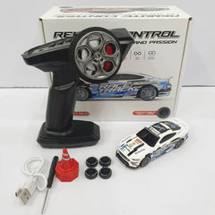 RC drift car beside its box and remote control, with spare wheels, a traffic cone, a screwdriver and a USB cable laid out