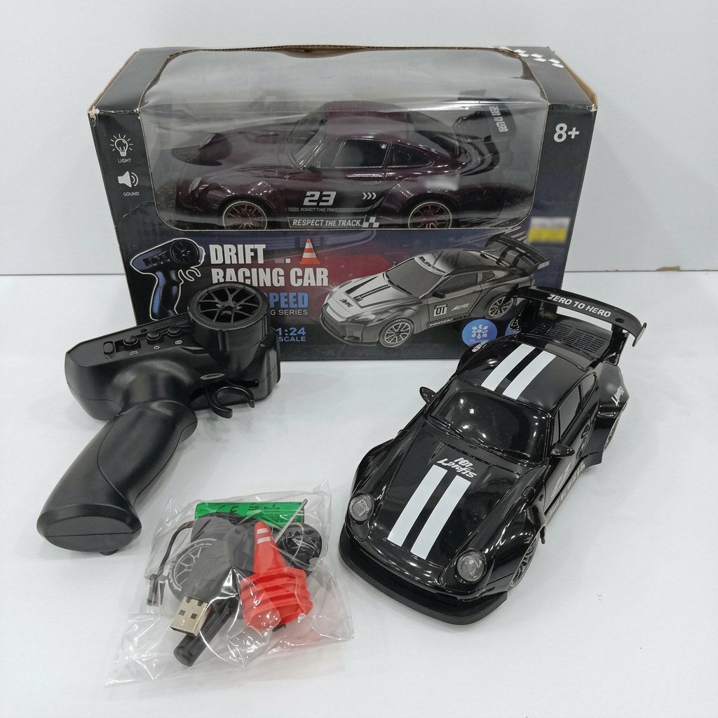 Black 1:24 drift RC car numbered 23, with its controller, spare wheel, traffic cone, battery pack and USB cable, beside the "8+" box